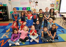 students lined up sitting and standing on mats in a classroom